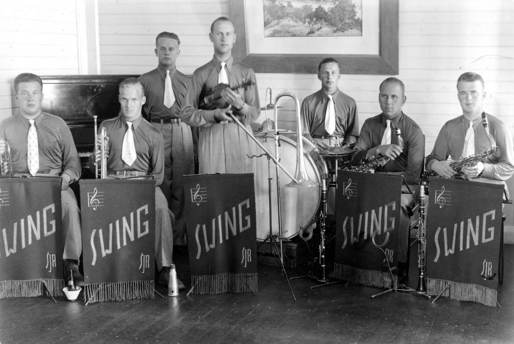 Mustavalkoisessa kuvassa näkyy seitsemän miehen bändi. Heidän edessään roikkuu kankaita, joissa lukee "SWING". Bändin jäsenet ovat pukeutuneet samalla tavalla.