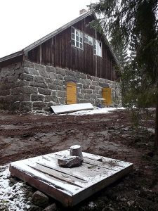 Alaosasta lohkokivisen navetan edessä on kaivo, joka on peitetty puukannella. Maa on tasattu kaivinkoneella, ja lunta on satanut vähän maahan.