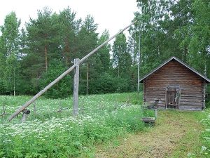 Maalaamattoman hirsisaunan edessä on matala puinen kaivonkehä ja kansi. Vieressä on kaivon vintti, jolla vettä on nostettu kaivosta.