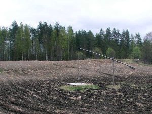 Kynnetyn pellon keskellä on kaivo pienellä kumpareella ja vieressä kaivon vintti.