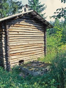 Hirsirakenteisen saunan päädyssä kivipuitekaivo, jonka kantena on iso, laakea kivi.