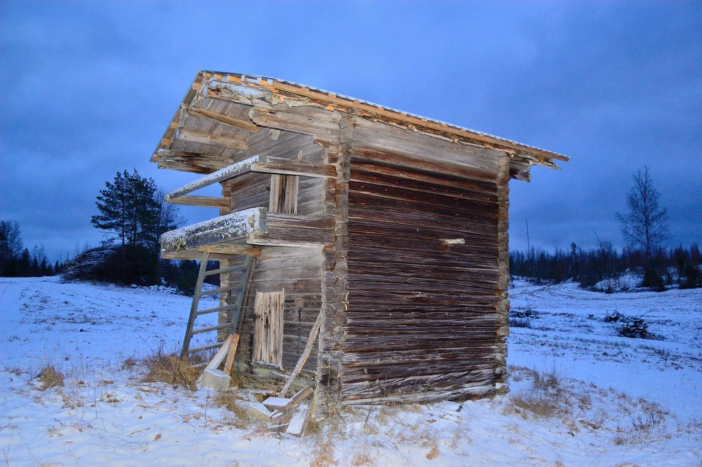 Osin lumenpeittämä kaksikerroksinen hirsirakennus, jossa on uusi peltikatto.