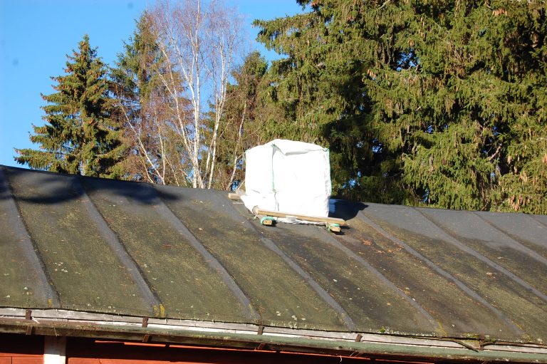 Musta huopakatto, jonka savupiippu on huputettu valkealle säkillä.