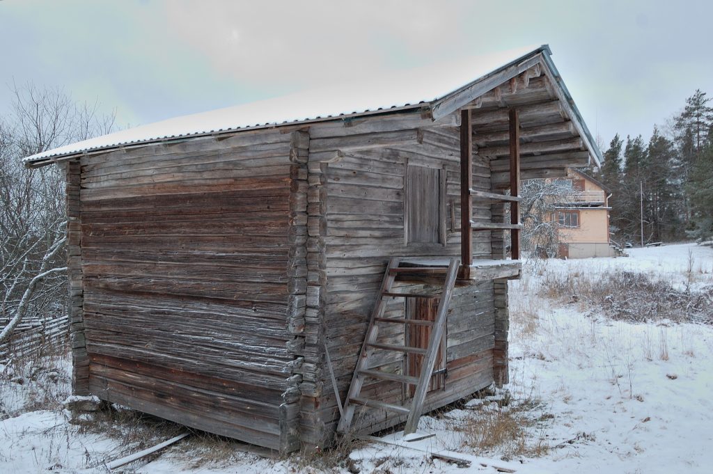 Osin lumenpeittämä kaksikerroksinen hirsirakennus, jossa on uusi peltikatto.