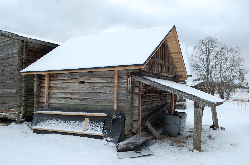 Osin lumenpeittämä hirsirakennus, jossa on uusi, musta saumahuopakate.