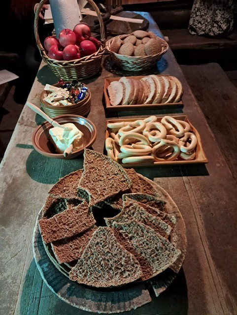 Puinen pöytä, jonka päällä on ruisleipää, voita, rinkeleitä ja omenia.