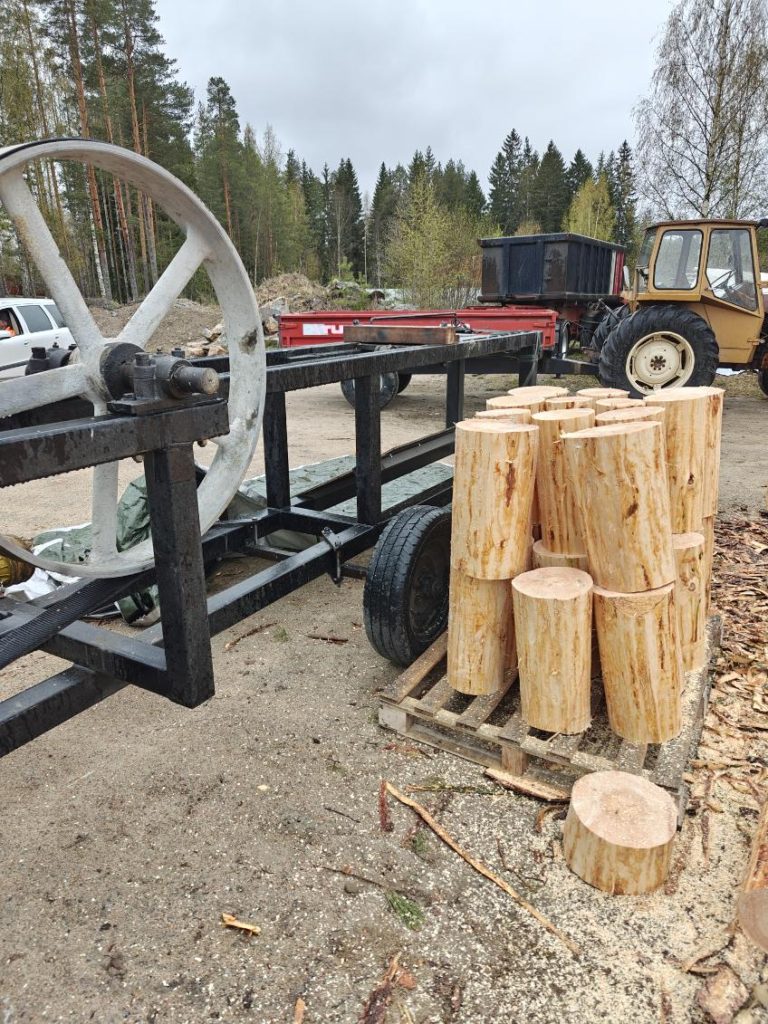 Katkottuja mäntypöllejä pystyssä trukkilavan päällä metallirunkoisen pärehöylän vieressä.