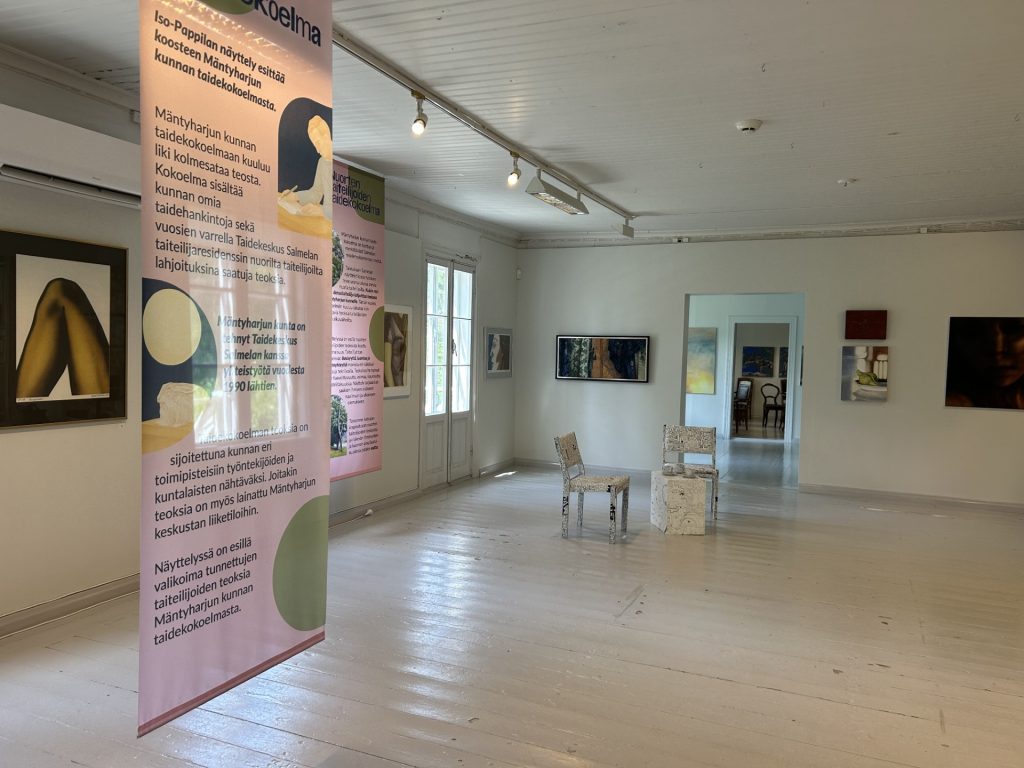 Pääasiassa ripustettavaa taidetta näyttelytilassa, jonka seinät ja lattia on maalattu vaaleaksi.