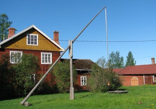 Pääasiassa punaiseksi maalattuja maatilan rakennuksia, joiden edessä on suuri puinen kaivon vintti ja matala kaivon kehän kansineen.