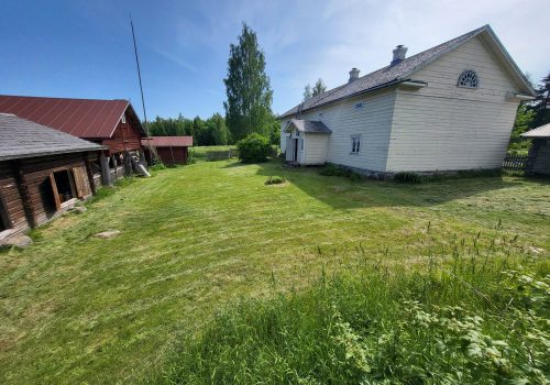 Maatalon pihanurmikko on leikattu. Vasemmalla valkeaksi maalattu päärakennus, ja vastapäätä navetta.