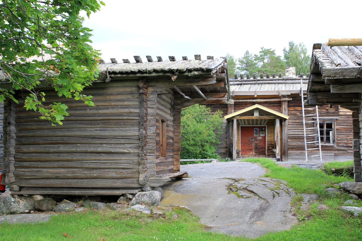 Kolme maalaamatonta hirsirakennusta. Kaikissa on katteena tuohi-malkakatto.