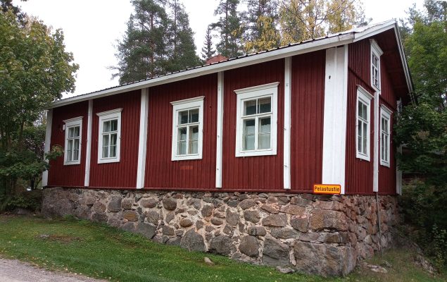 Korkean, luonnonkivistä muuratun perustuksen päälle pystytetty hirsirakennus, jonka vuori on maalattu punaiseksi.