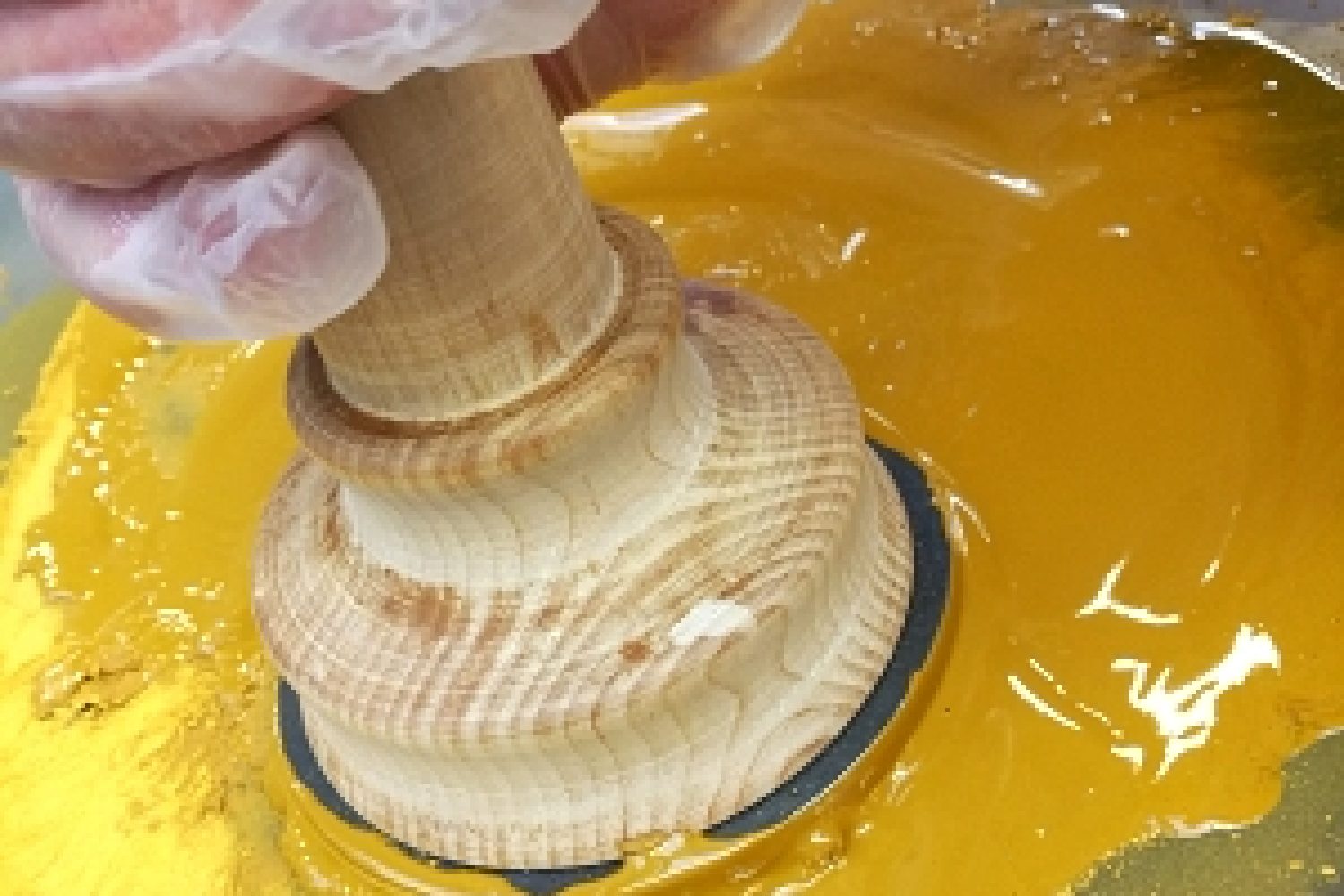 Lasilevyn päällä hierretään käsin puuvartisella hiertimellä keltaista pigmenttiä ja vernissaa maalitahnaksi. Pellavaöljymaalin valmistamista.