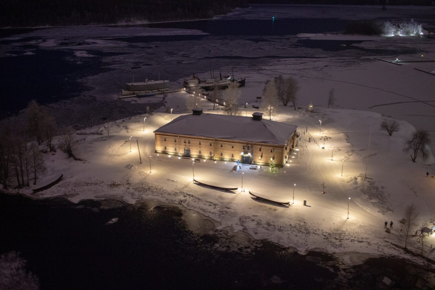 Linnan tornista otettu talvikuva Riihisaaresta: lunta maassa ja museorakennus valaistuna.