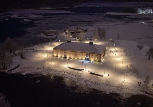 Linnan tornista otettu talvikuva Riihisaaresta: lunta maassa ja museorakennus valaistuna.