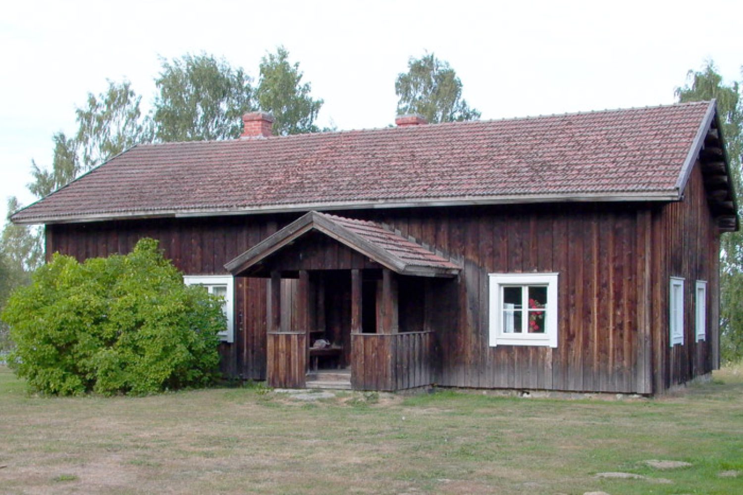 Ulkokuva Rantasalmen museon päärakennuksesta, joka on pystysuunnassa lauta-rimavuorattu hirsirakennus avokuistilla ja sementtitiilikatolla.