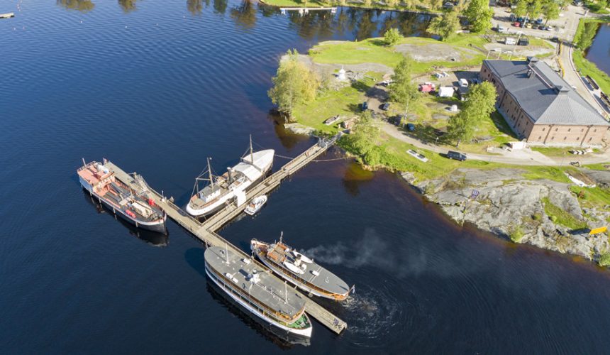 Kesäinen ilmakuva neljästä laivasta kiinnittyneenä T-kirjaimen muotoiseen laituriin.